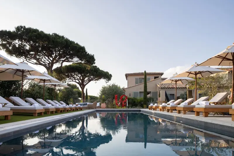 Transats blancs alignés au bord d'une piscine rectangulaire sous des parasols.