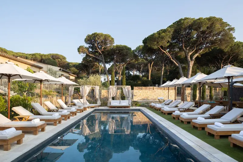Transats blancs disposés autour d'une piscine rectangulaire sous des parasols.