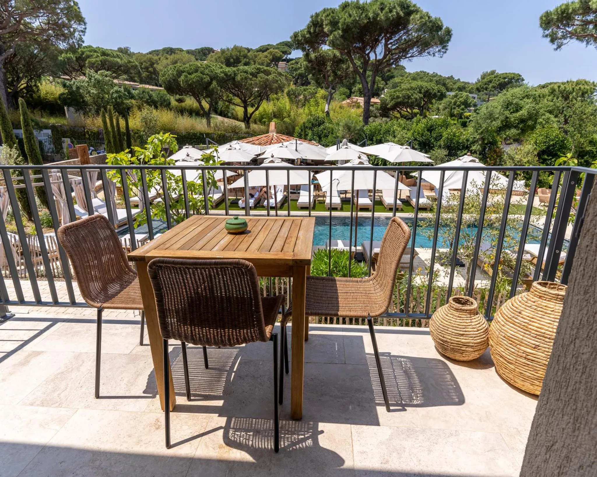 Terrasse avec mobilier en osier et vue sur une piscine et des transats.