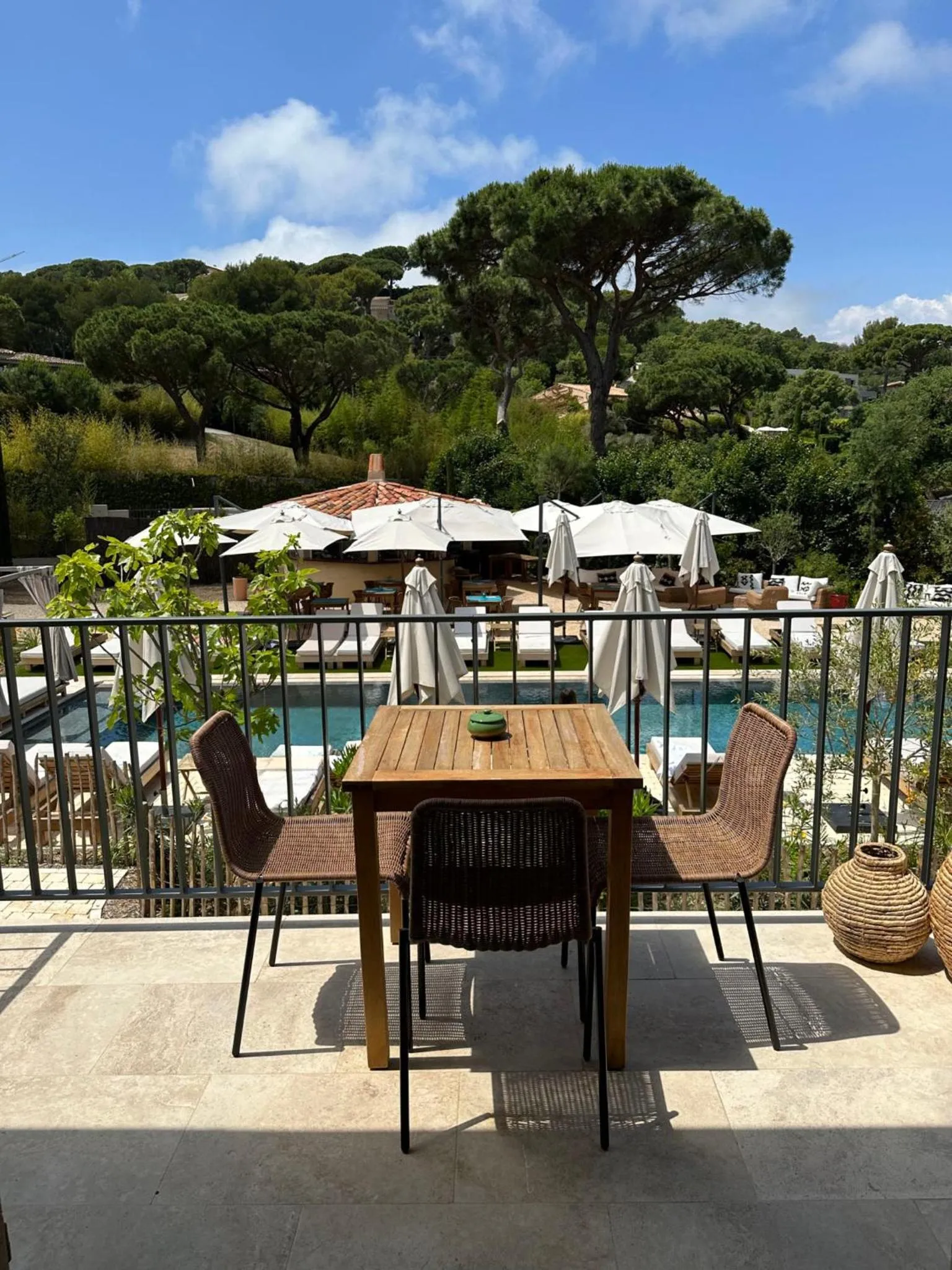 Terrasse avec table et chaises donnant sur une piscine et un espace de détente ombragé.