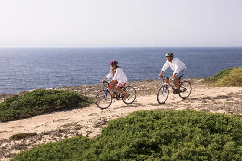 Un couple fait du vélo sur un sentier côtier ensoleillé avec vue sur la mer.