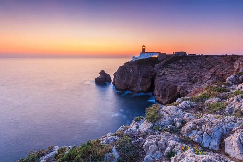 Phare perché sur une falaise surplombant la mer au coucher du soleil.