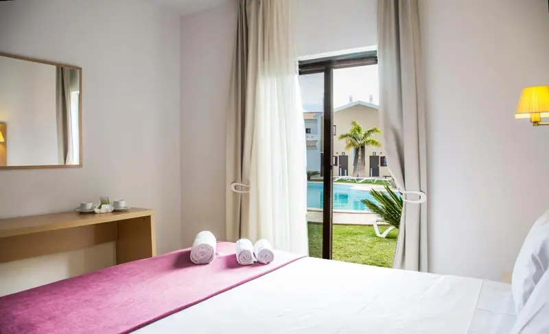 Une chambre lumineuse avec un lit recouvert d'une courtepointe rose et une vue sur une piscine.