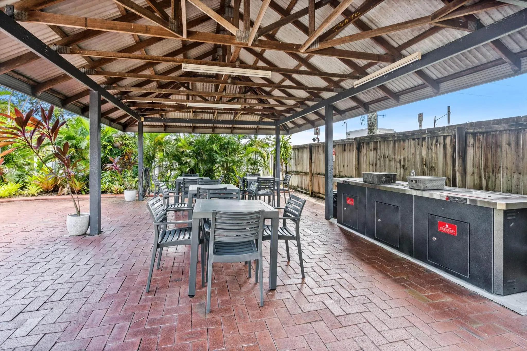 Espace extérieur couvert avec tables, chaises et barbecues.