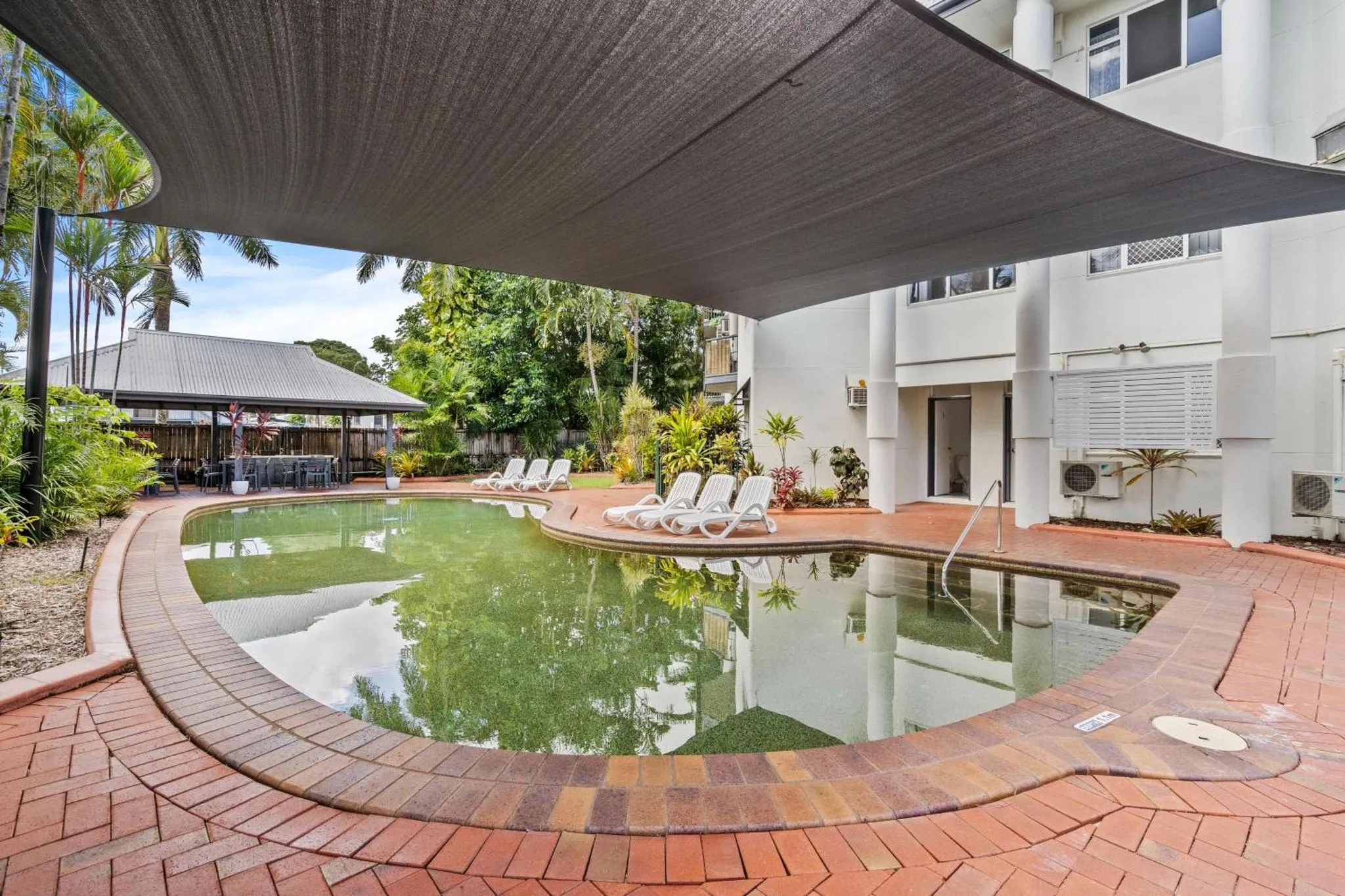 Piscine rectangulaire entourée d'une terrasse pavée et ombragée.