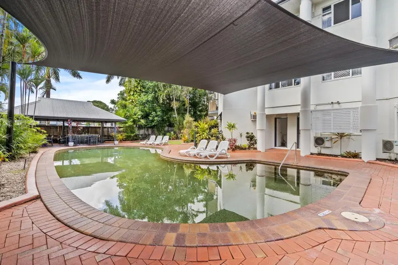 Piscine rectangulaire entourée d'une terrasse pavée et ombragée.