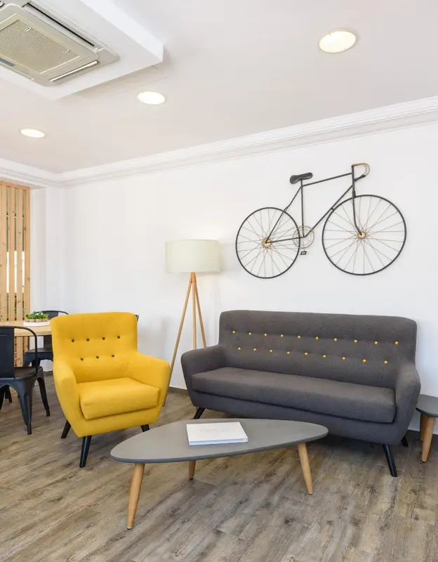 Un salon clair avec un canapé gris, un fauteuil jaune et un vélo décoratif au mur.