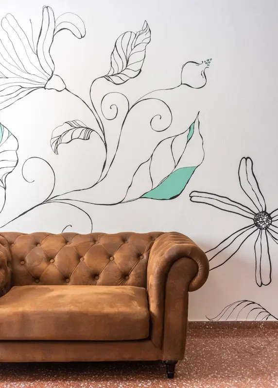 Un canapé en cuir marron est placé devant un mur décoré de motifs végétaux stylisés.