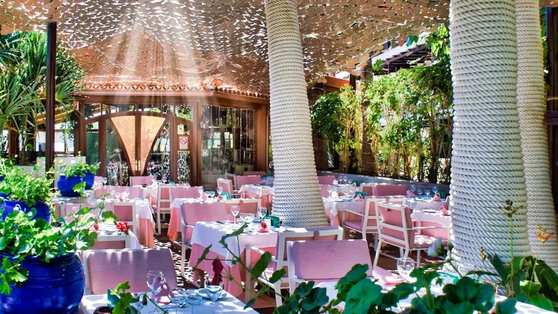 Une salle à manger lumineuse avec des tables dressées et une végétation luxuriante.