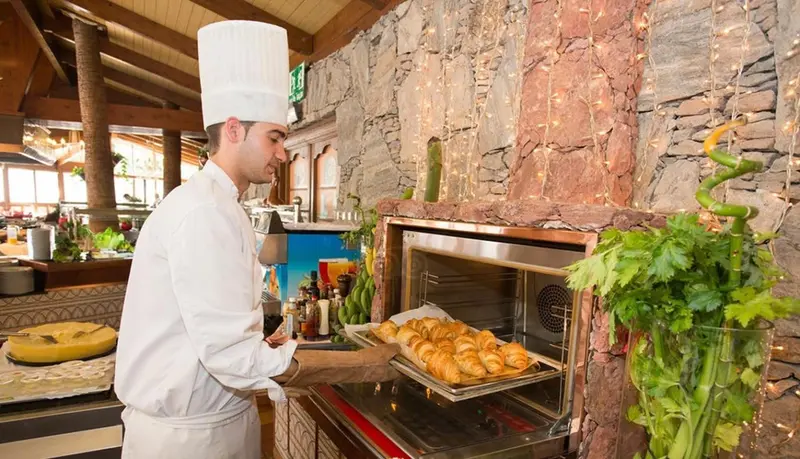 Un chef de cuisine sort une plaque de viennoiseries d'un four en pierre.
