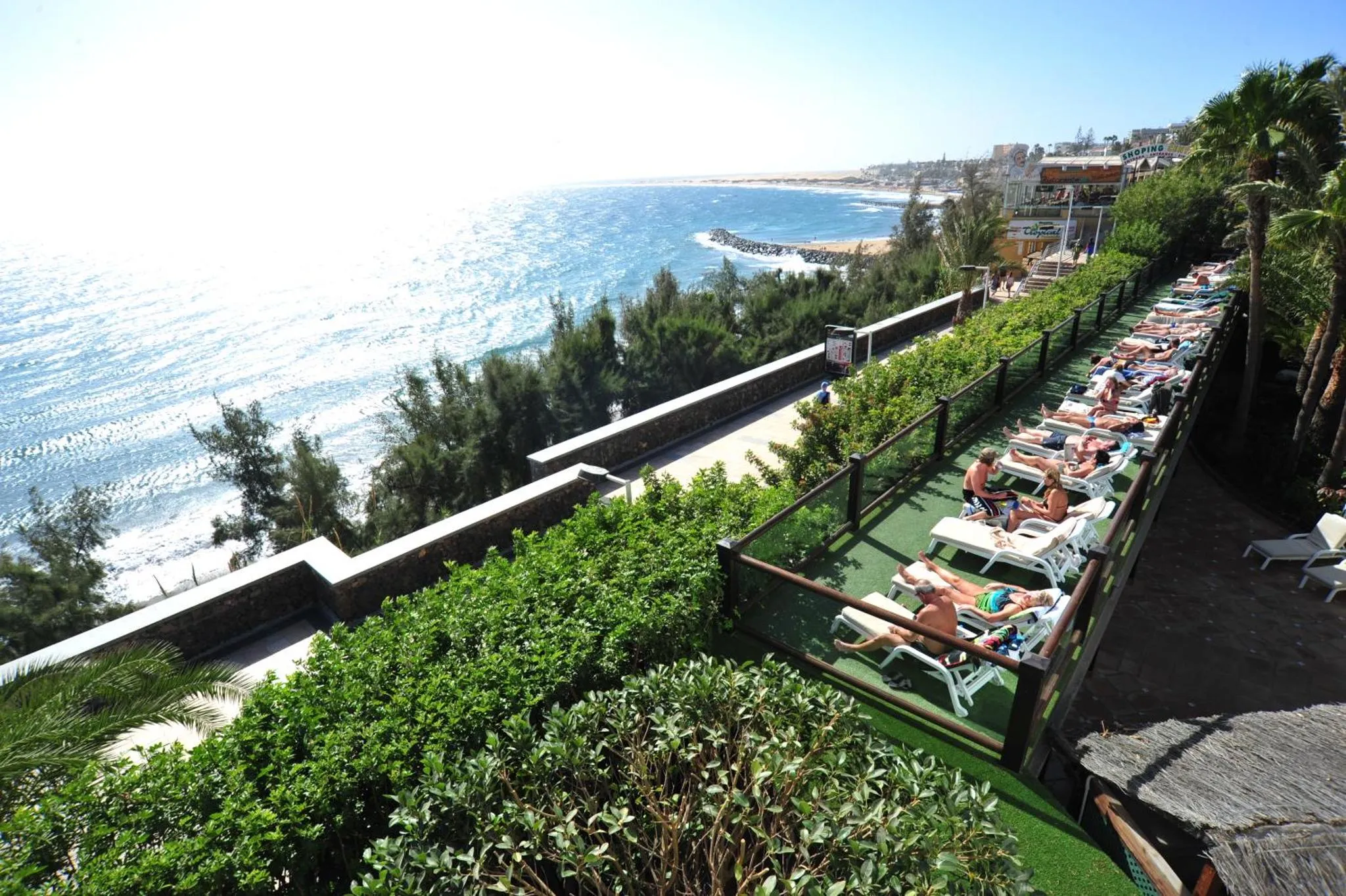Terrasse ensoleillée avec transats et vue sur la mer.
