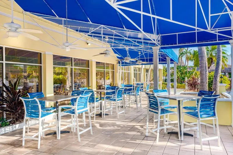 Terrasse ombragée avec tables et chaises bleues sous une structure architecturale.