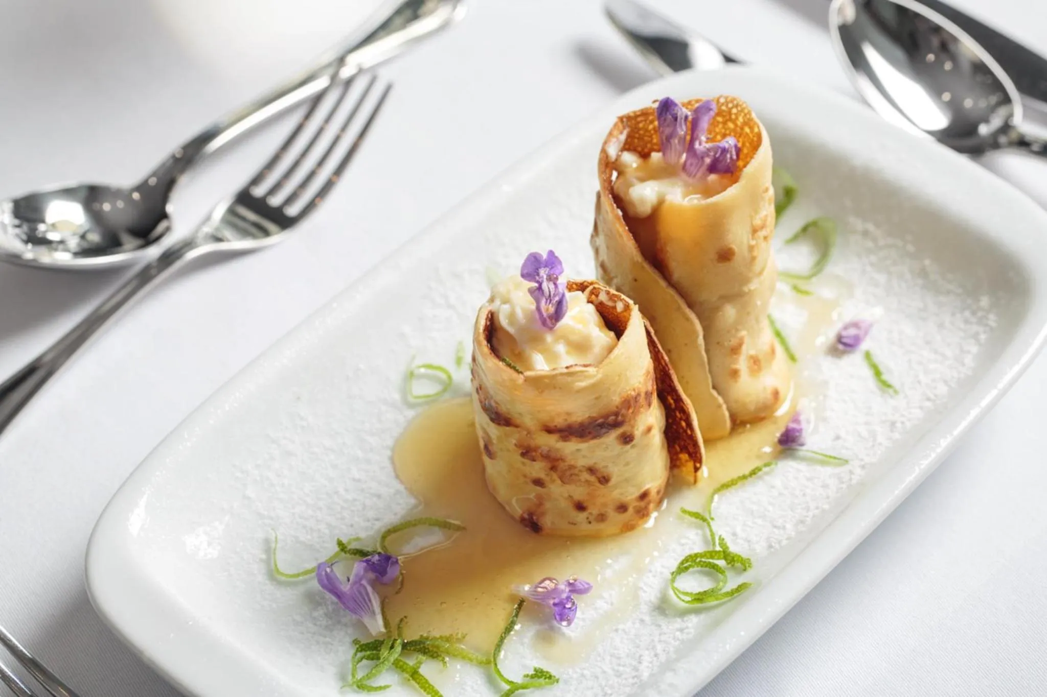 Assiette de crêpes fines garnies et décorées de fleurs, nappée d'une sauce dorée.