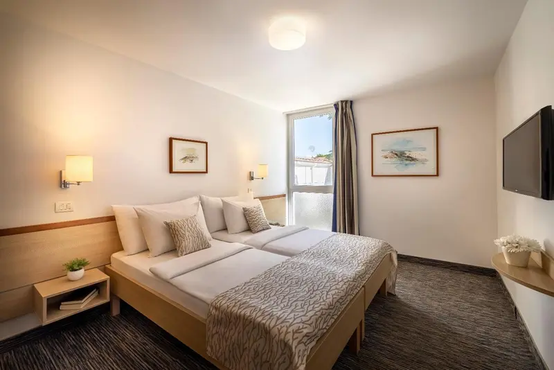 Chambre lumineuse avec deux lits simples et une fenêtre.