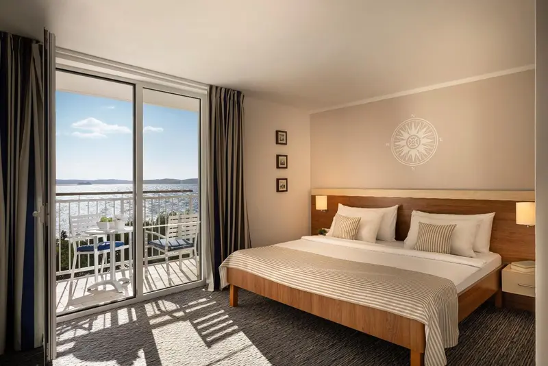 Chambre lumineuse avec un grand lit et une vue sur la mer depuis un balcon.