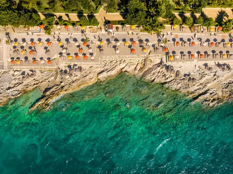 Vue aérienne d'une plage avec des transats et parasols le long d'une côte rocheuse.