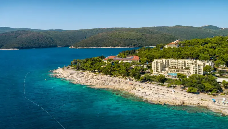 Vue aérienne d'un complexe hôtelier au bord d'une crique rocheuse et d'une mer turquoise.