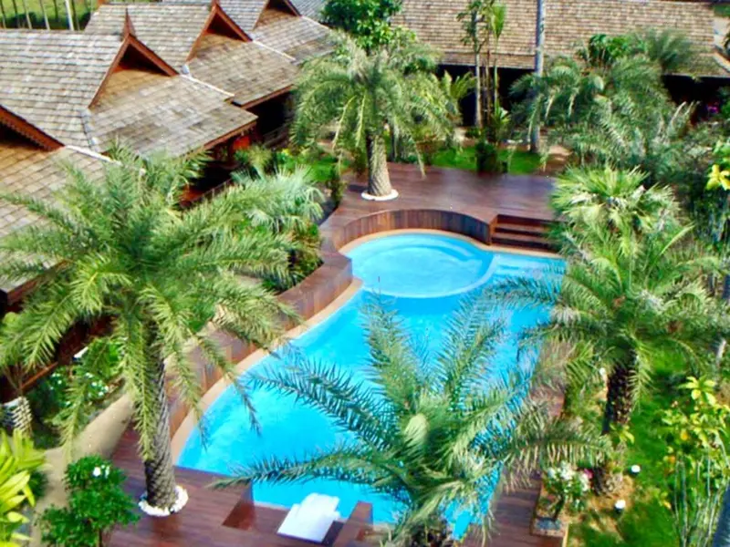 Vue aérienne d'une piscine entourée de végétation tropicale et de bâtiments.