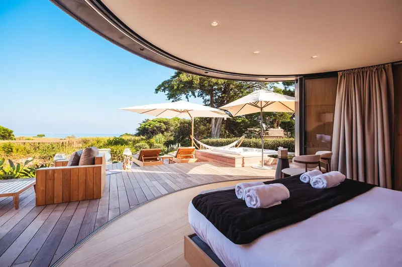 Une chambre spacieuse s'ouvre sur une terrasse avec jacuzzi et vue sur la végétation.