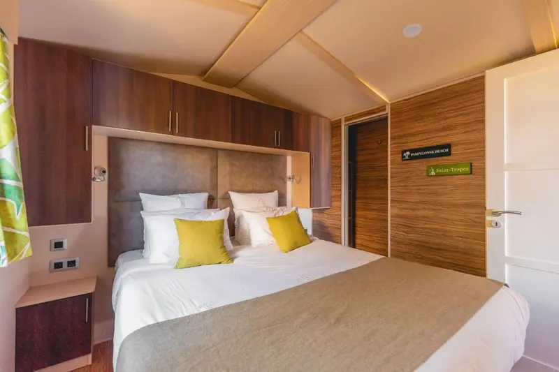 Une chambre lumineuse avec un grand lit recouvert d'une courtepointe blanche et de coussins jaunes.