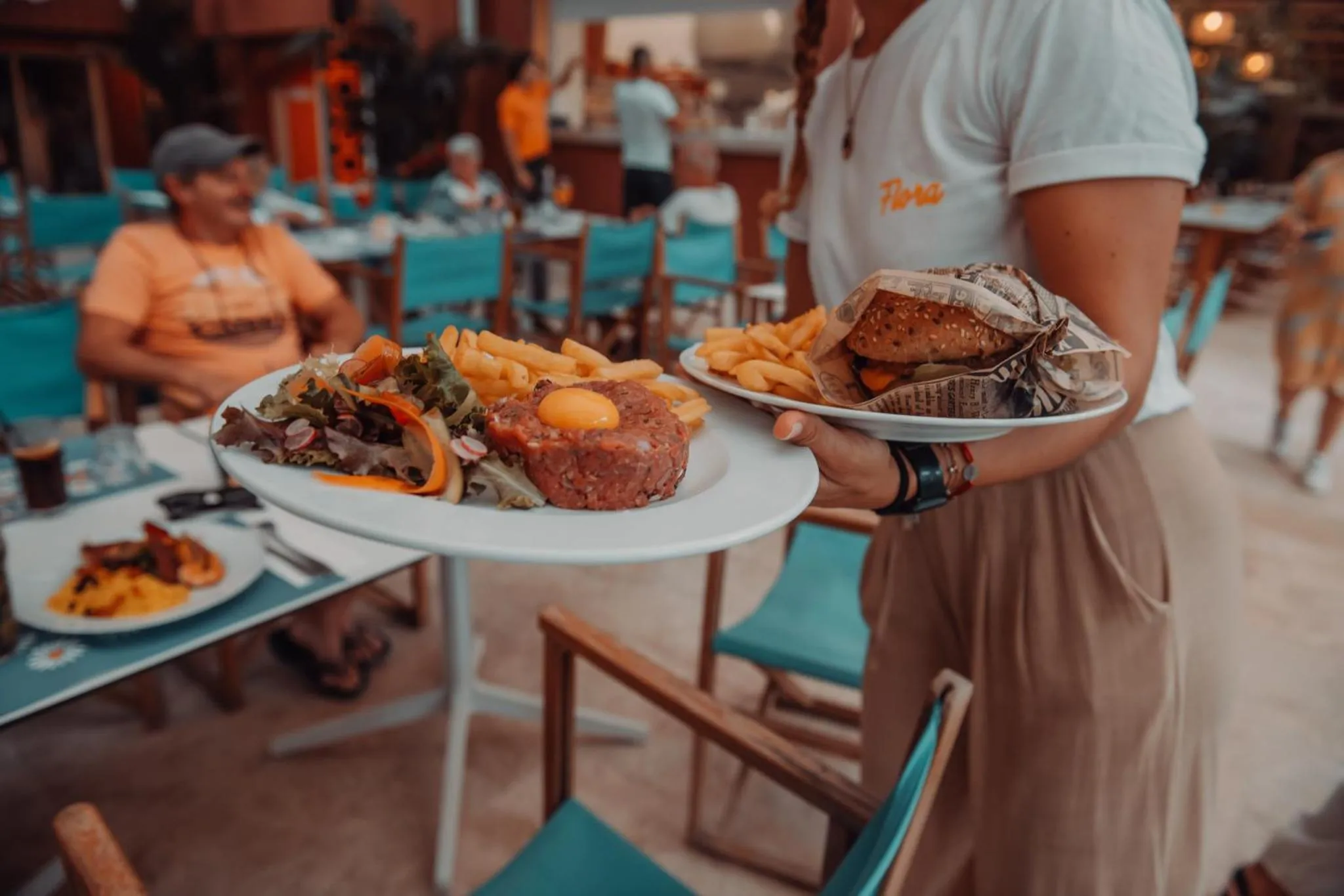 Un serveur porte une grande assiette de nourriture à un client attablé en terrasse.