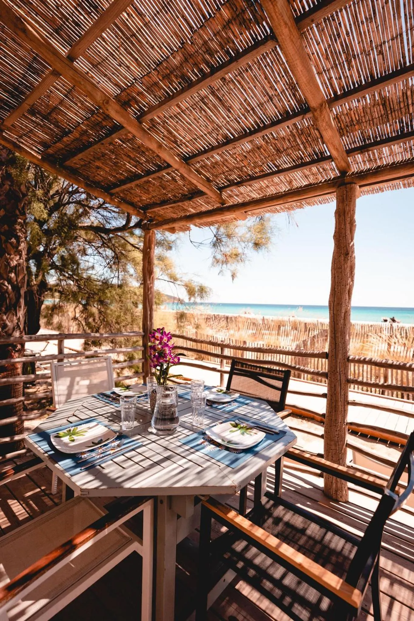 Une table est dressée sur une terrasse ombragée avec vue sur la mer.