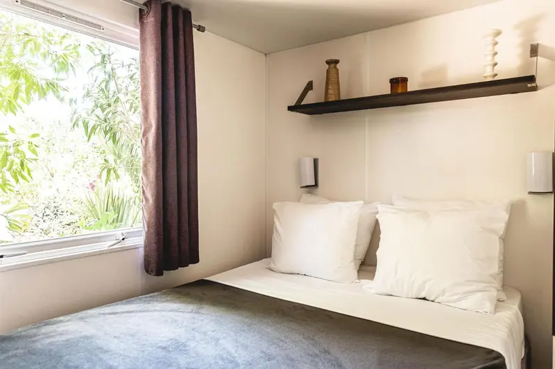 Une chambre lumineuse avec un lit simple et une vue sur la végétation.