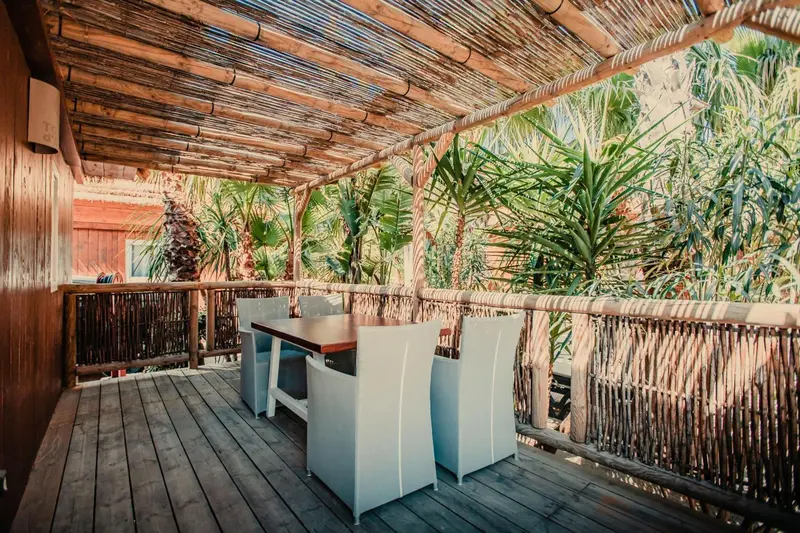 Une terrasse en bois abritée par un toit de chaume, avec des tables et des chaises.