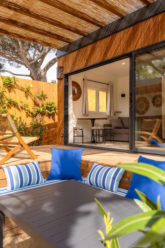 Terrasse aménagée avec des coussins et des fauteuils devant une baie vitrée.