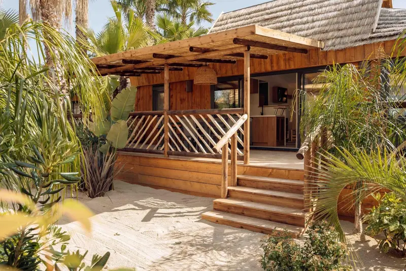 Une terrasse en bois donne accès à un bungalow avec une grande baie vitrée.
