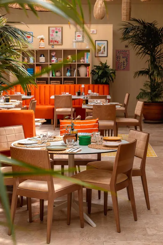 Une salle de restaurant lumineuse avec des tables dressées et des banquettes orange.