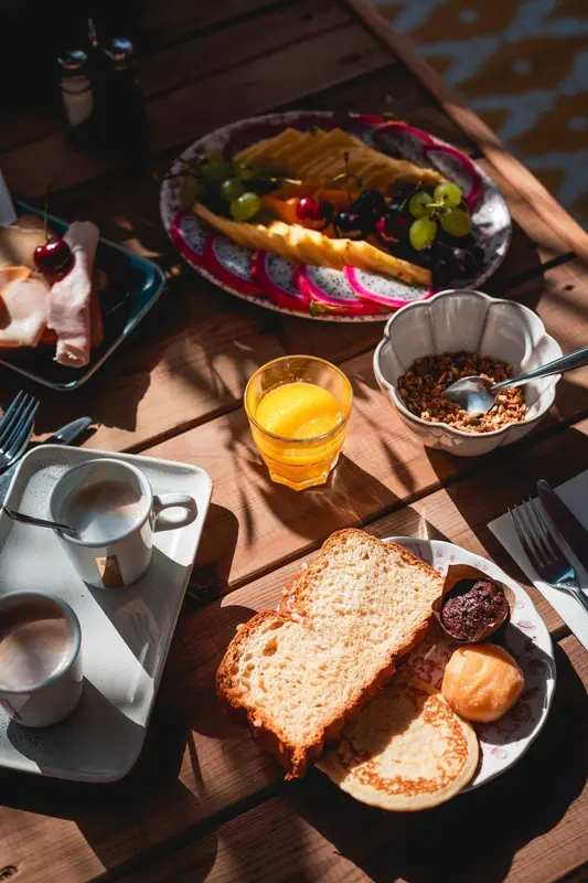 Une table en bois présente un petit-déjeuner avec des fruits, du pain et des boissons.