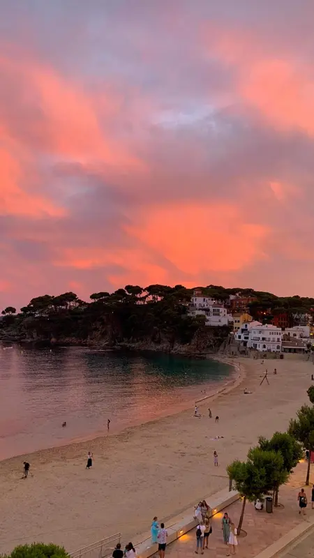 Une plage de sable fin bordée d'une eau turquoise sous un ciel rose orangé au coucher du soleil.