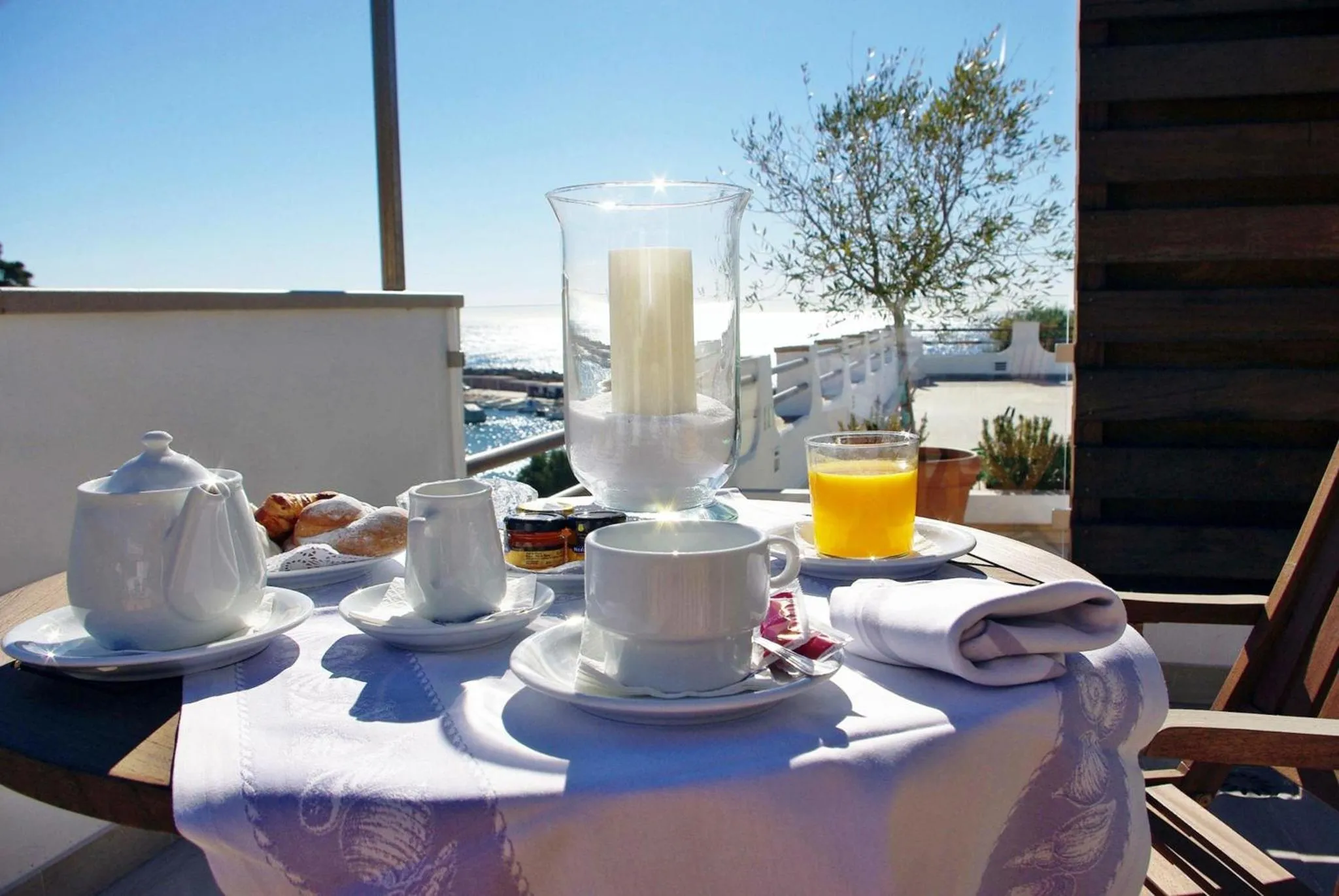 Une table est dressée pour le petit-déjeuner sur une terrasse ensoleillée avec vue sur la mer.