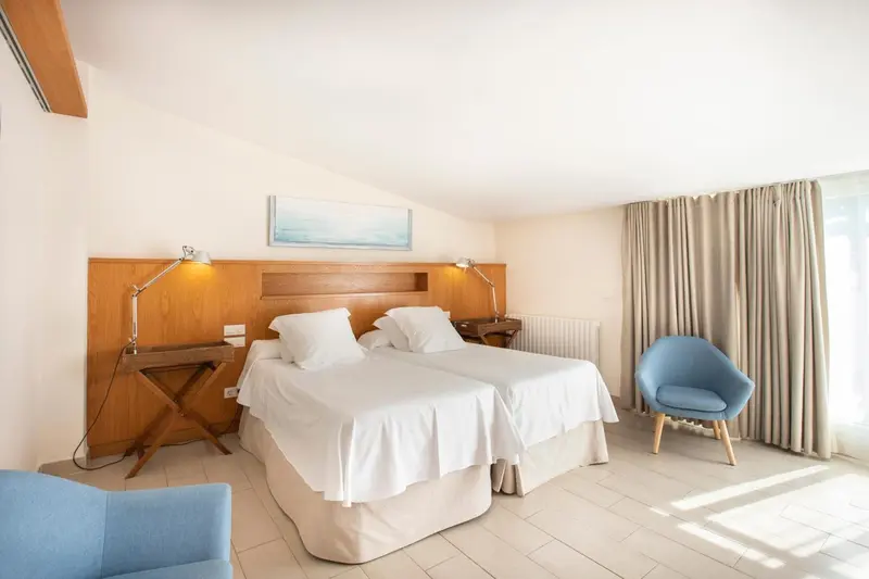 Une chambre lumineuse avec deux lits simples et un fauteuil bleu.