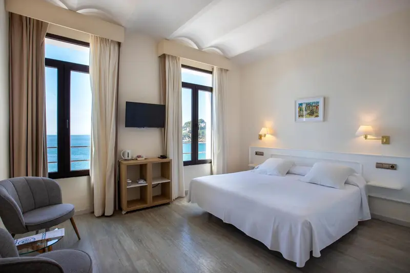 Chambre lumineuse avec un lit blanc et une vue sur la mer.