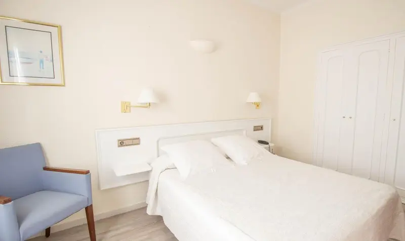 Une chambre lumineuse avec un lit double et un fauteuil.