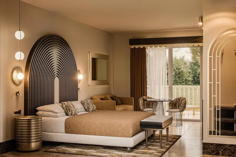 Une chambre à coucher lumineuse avec un grand lit et un coin salon donnant sur une terrasse.