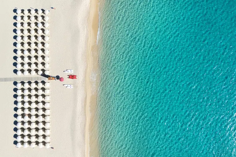 Vue aérienne d'une plage avec des transats alignés et une mer turquoise.