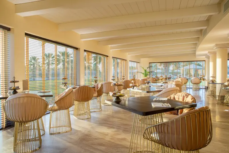 Une salle lumineuse avec des tables basses et des fauteuils confortables offre une vue sur un jardin tropical.