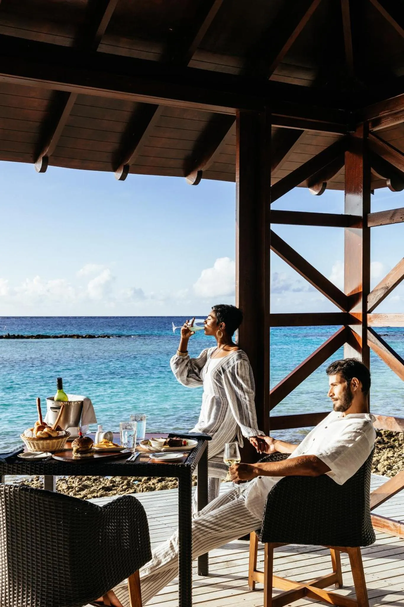 Un couple déguste des boissons et des en-cas sur une terrasse face à la mer.
