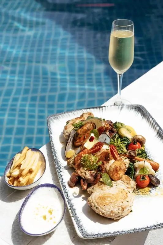 Un plat de fruits de mer et de frites est servi avec une boisson sur une table près d'une piscine.