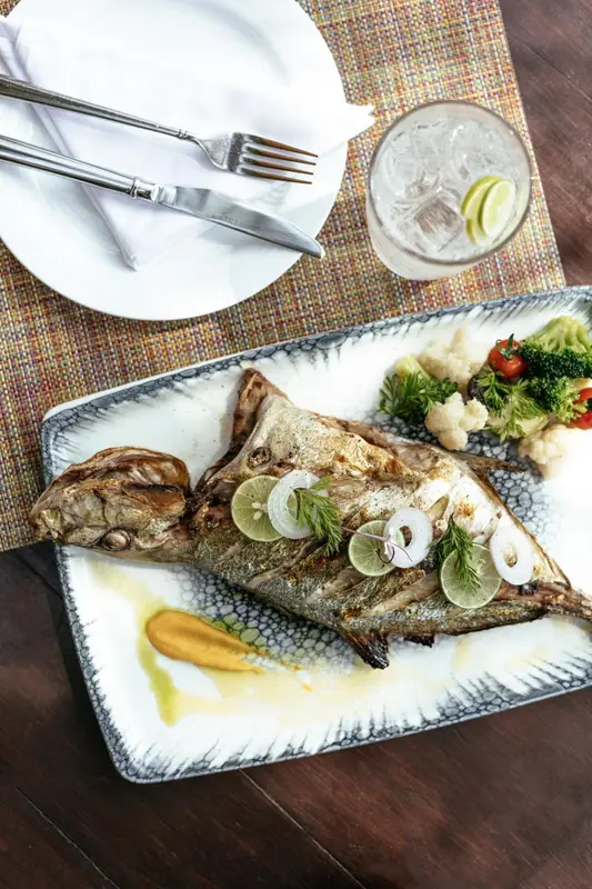 Un poisson grillé entier est servi avec des légumes et une sauce sur une assiette décorative.