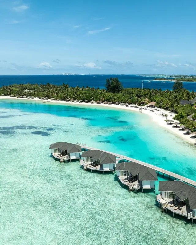 Vue aérienne d'un lagon turquoise bordé de bungalows sur pilotis et d'une plage de sable blanc.