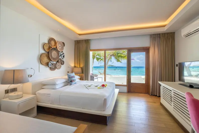 Une chambre lumineuse avec un grand lit donnant sur une plage tropicale.