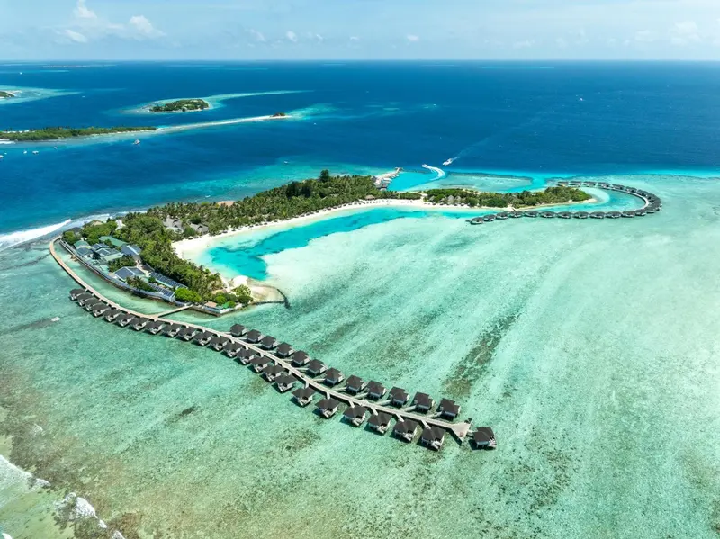 Vue aérienne d'une île tropicale avec des bungalows sur pilotis et une plage de sable blanc.