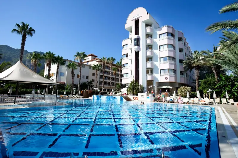 Vue d'une piscine d'hôtel avec des transats et des palmiers sous un ciel bleu.