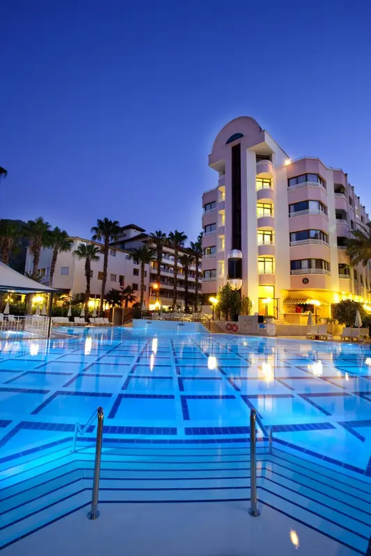 Bâtiment blanc illuminé au bord d'une piscine bleue la nuit.