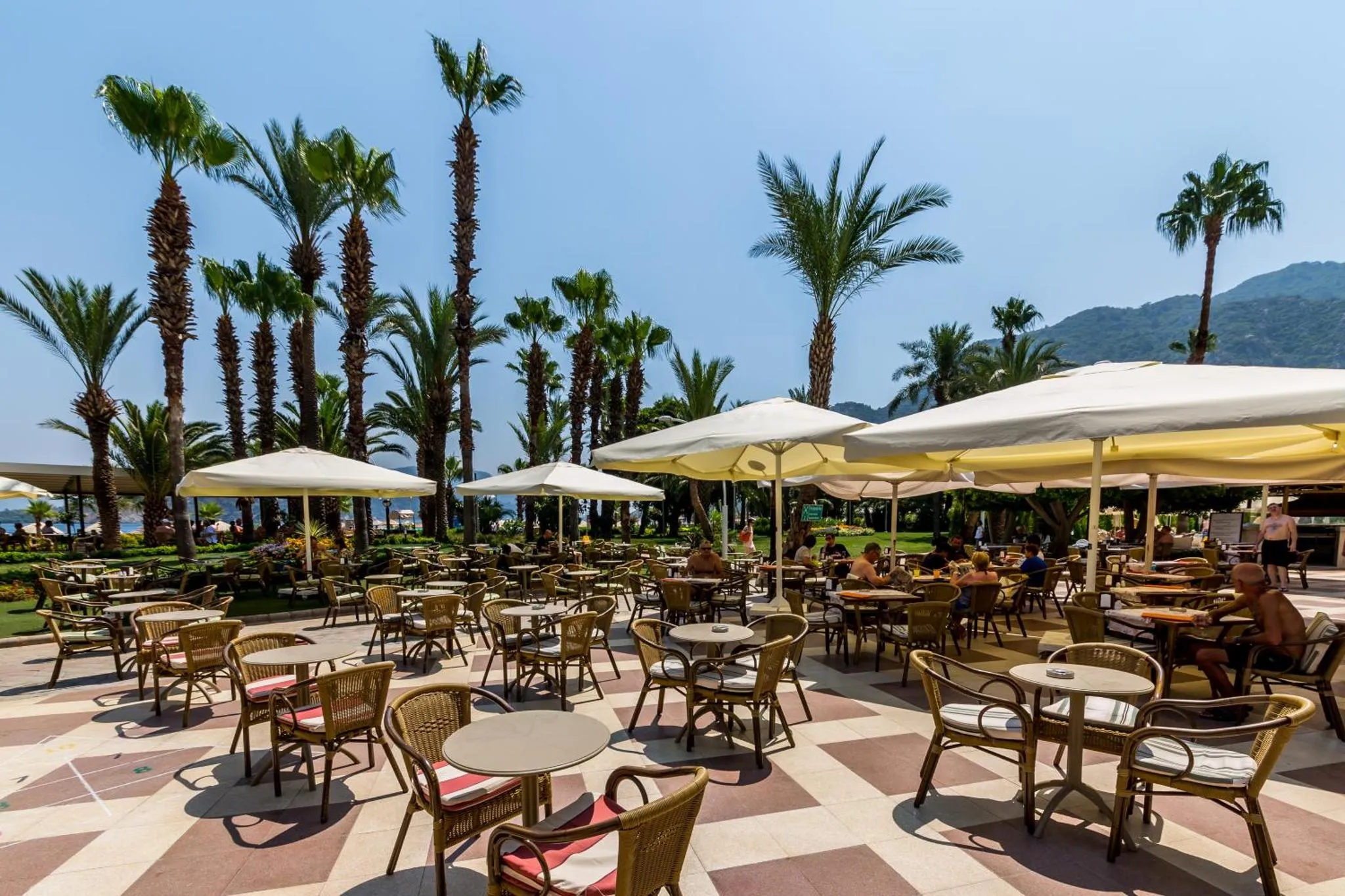 Terrasse ombragée avec tables et chaises près d'une plage de sable.
