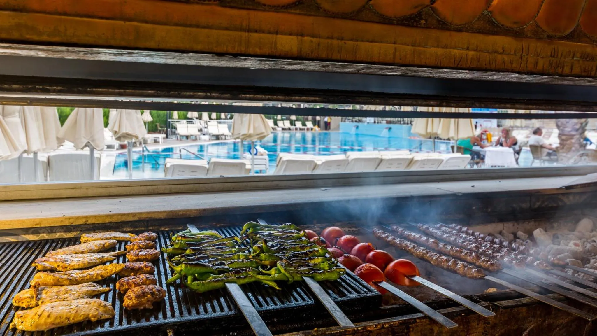 Des brochettes de viande et des légumes grillés sont préparés sur un barbecue en extérieur.